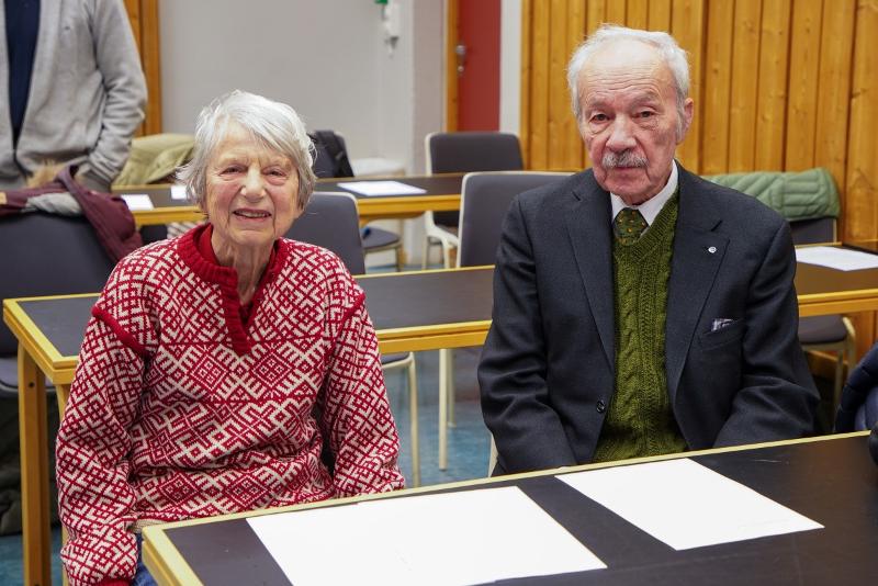 Ein eldre kvinne og ein eldre mann sit ved ein pult